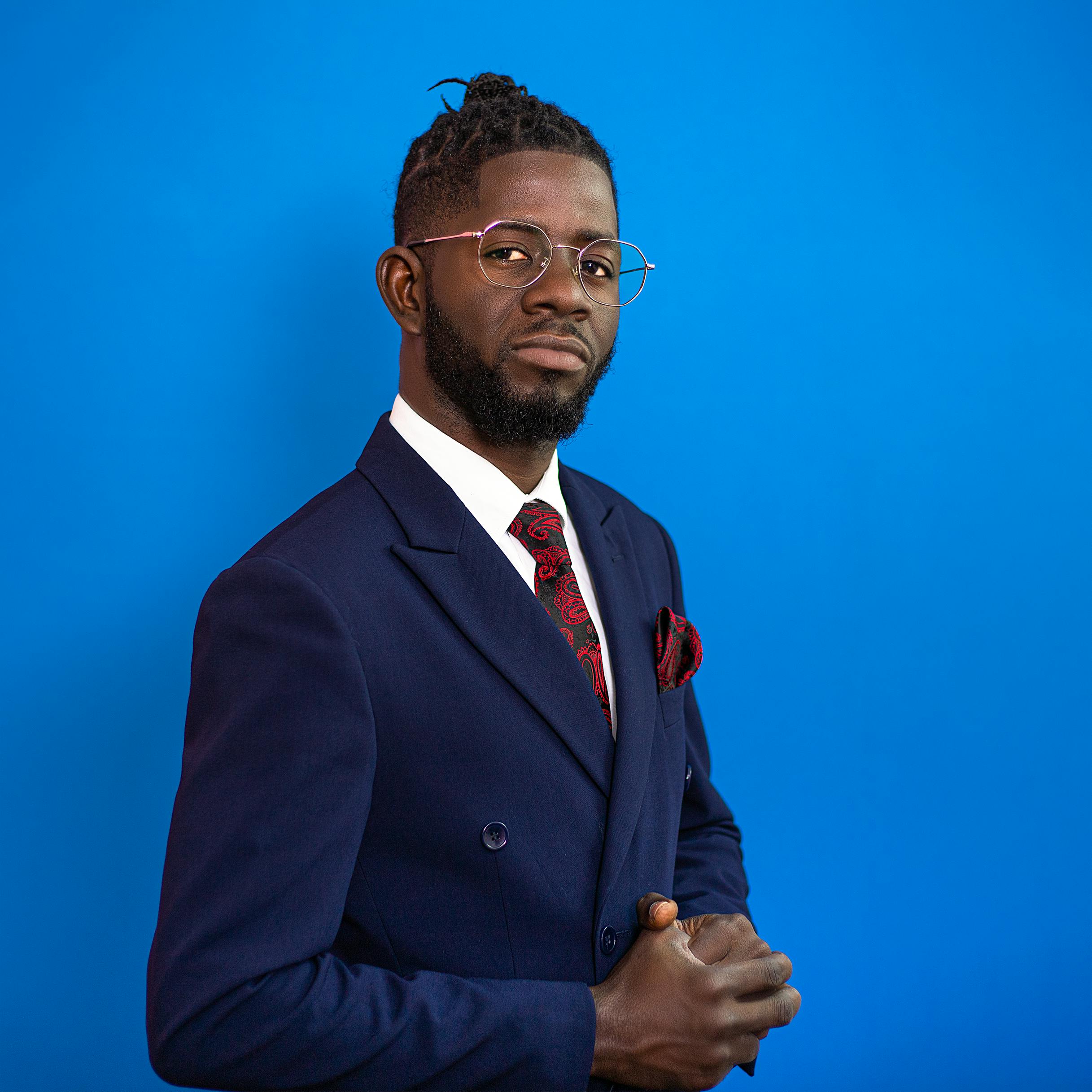 Confident man in a suit poses against a vibrant blue background.